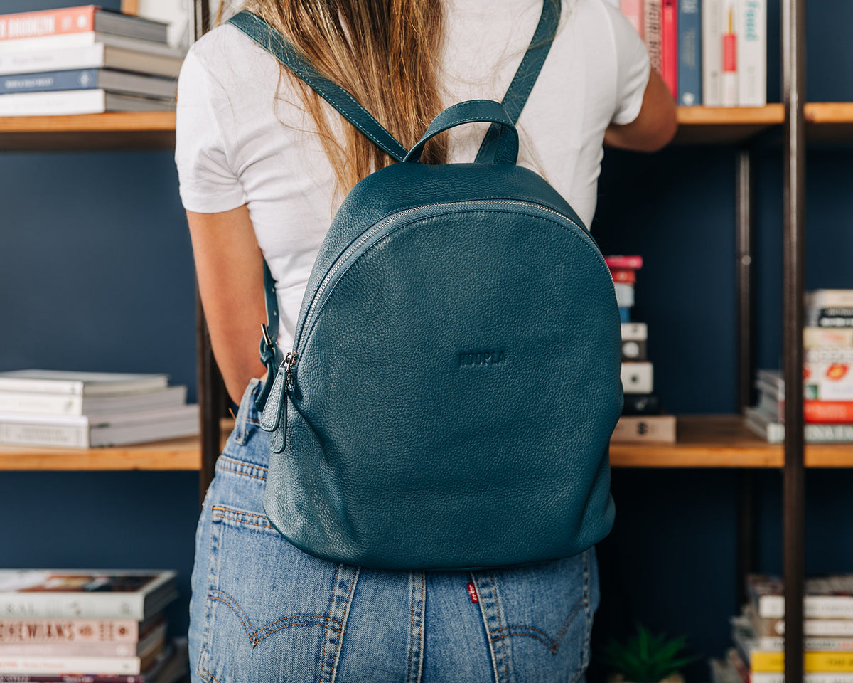 Model wearing Hoopla teal backpack, made from pebbled leather with with two adjustable straps and silver zips and buckles. Lined with striped cotton lining, hidden pocket on the base. 